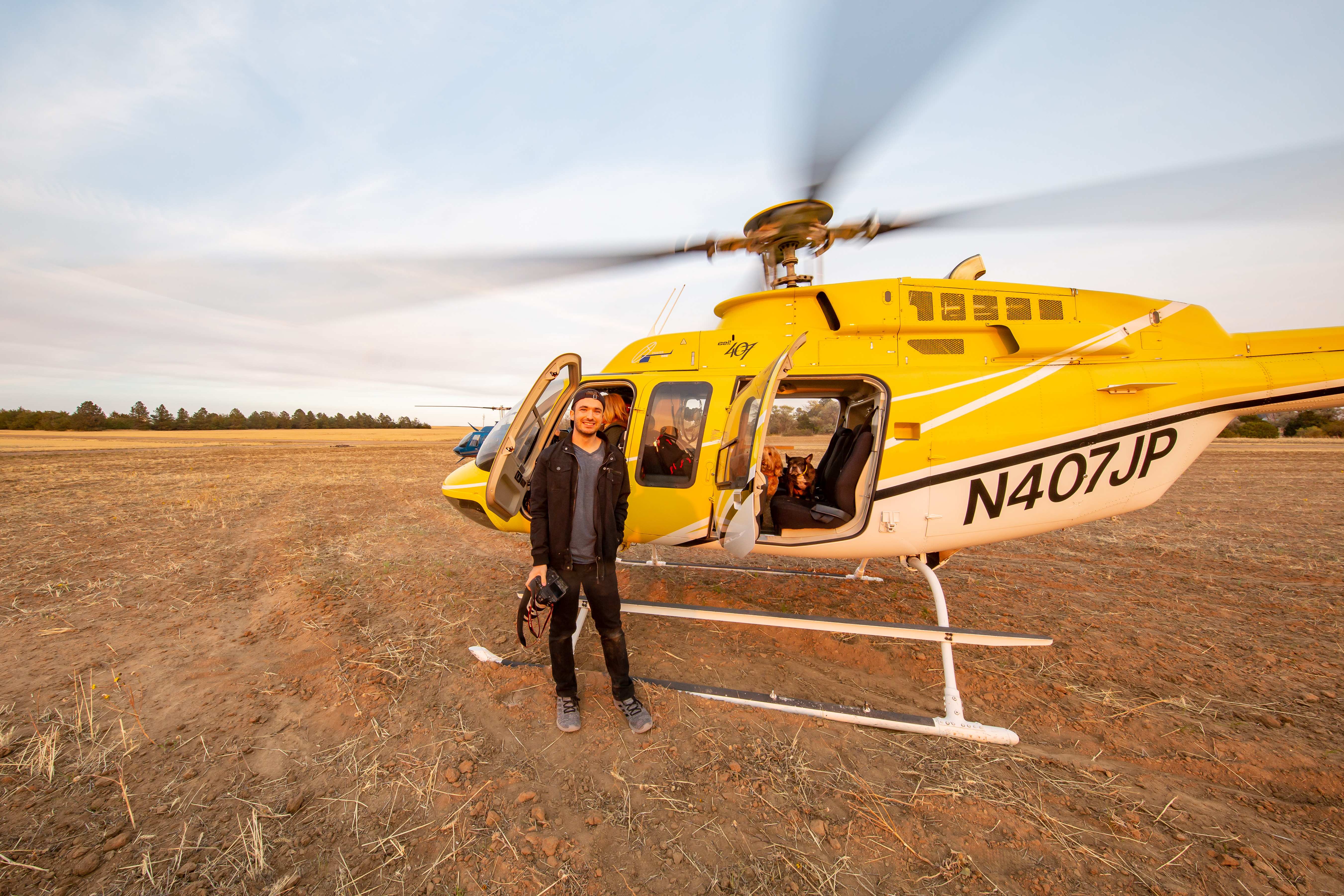Billy Hardiman standing beside a Bell 407 helicopter before aerial photography Billy Hardiman standing by yellow Bell 407 helicopter with rotors spinning