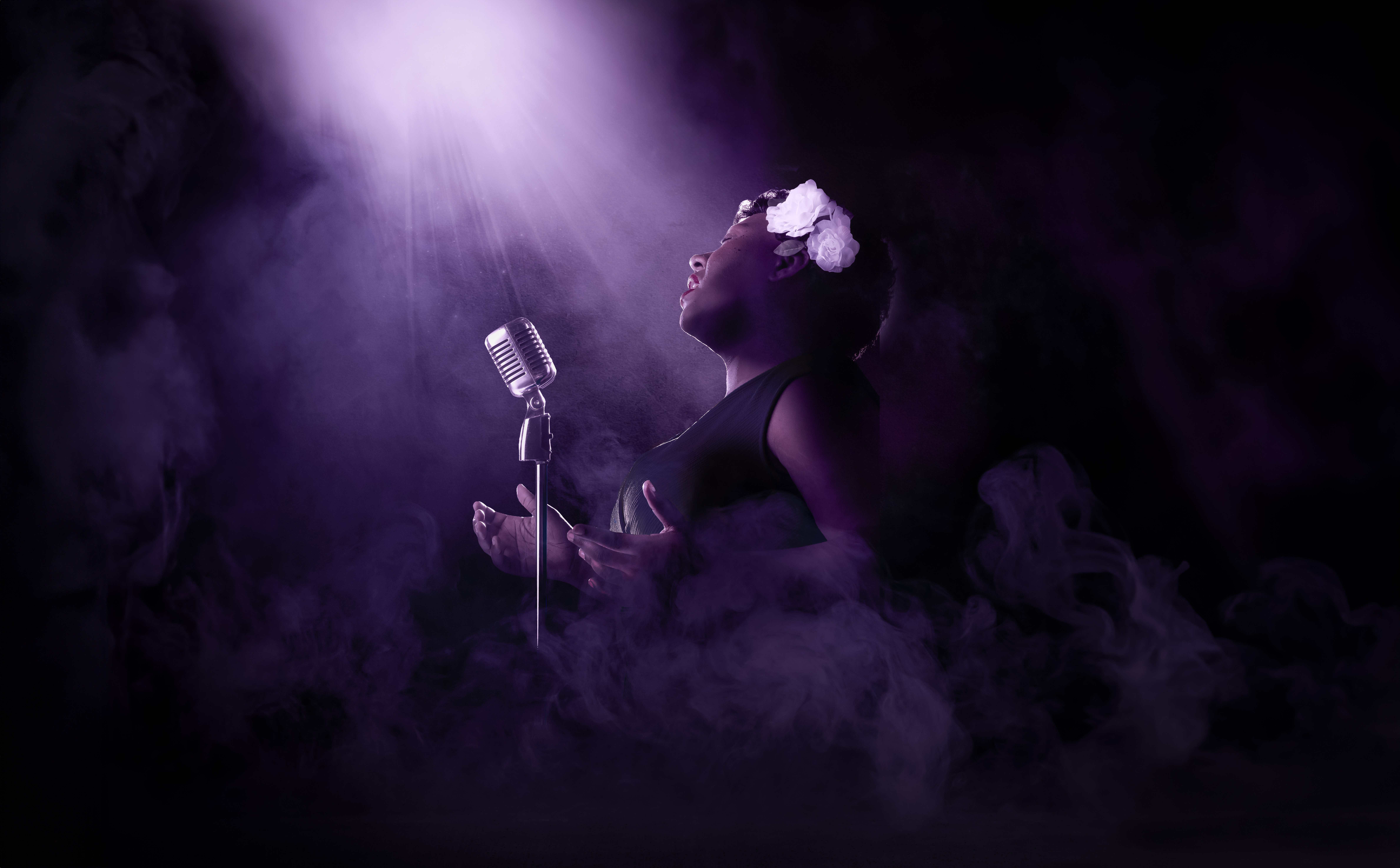 African-American female jazz singer performing with vintage microphone in studio with purple lighting