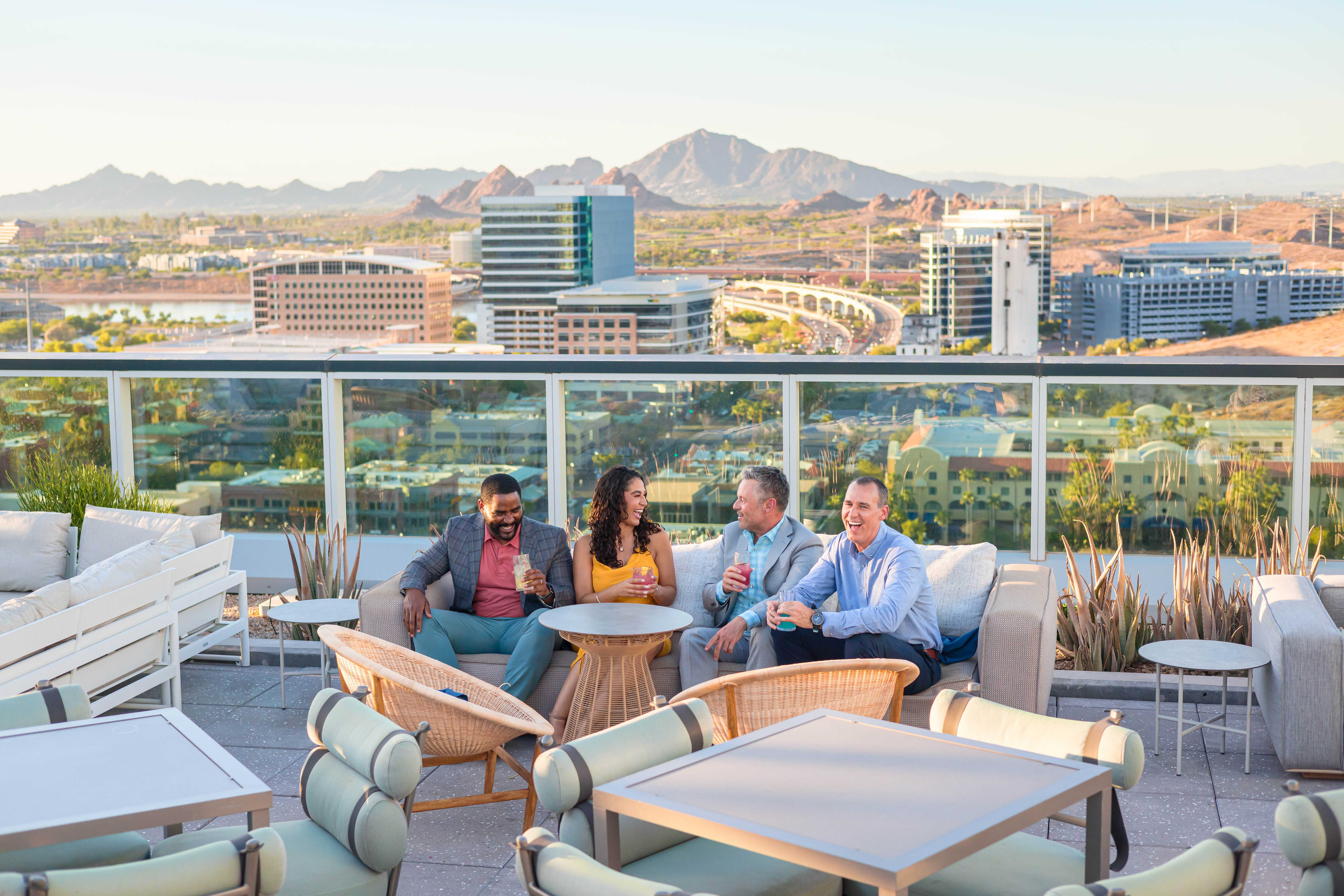 Well-dressed group of friends enjoying drinks at Skysill Rooftop Lounge with views of downtown Tempe and Camelback Mountain